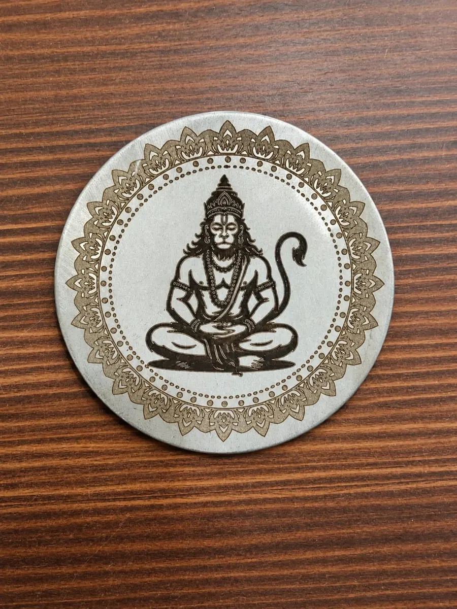 Decorative Hanuman engraving and patterned border on a round metal disc